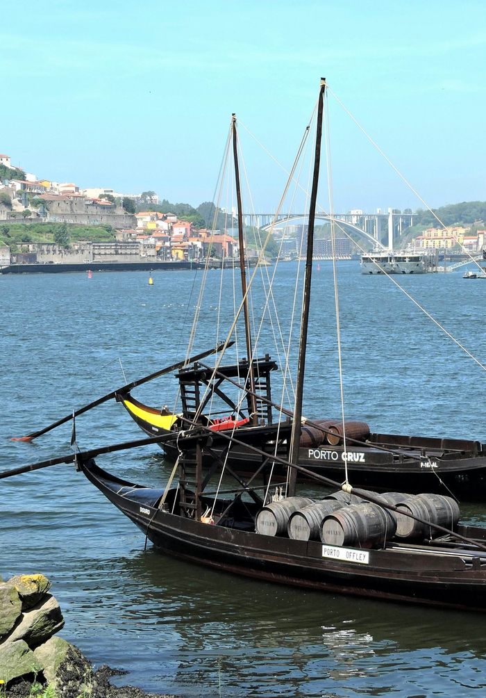 Scenic view of traditional boats on Douro River near Porto with a bridge and colorful houses.
