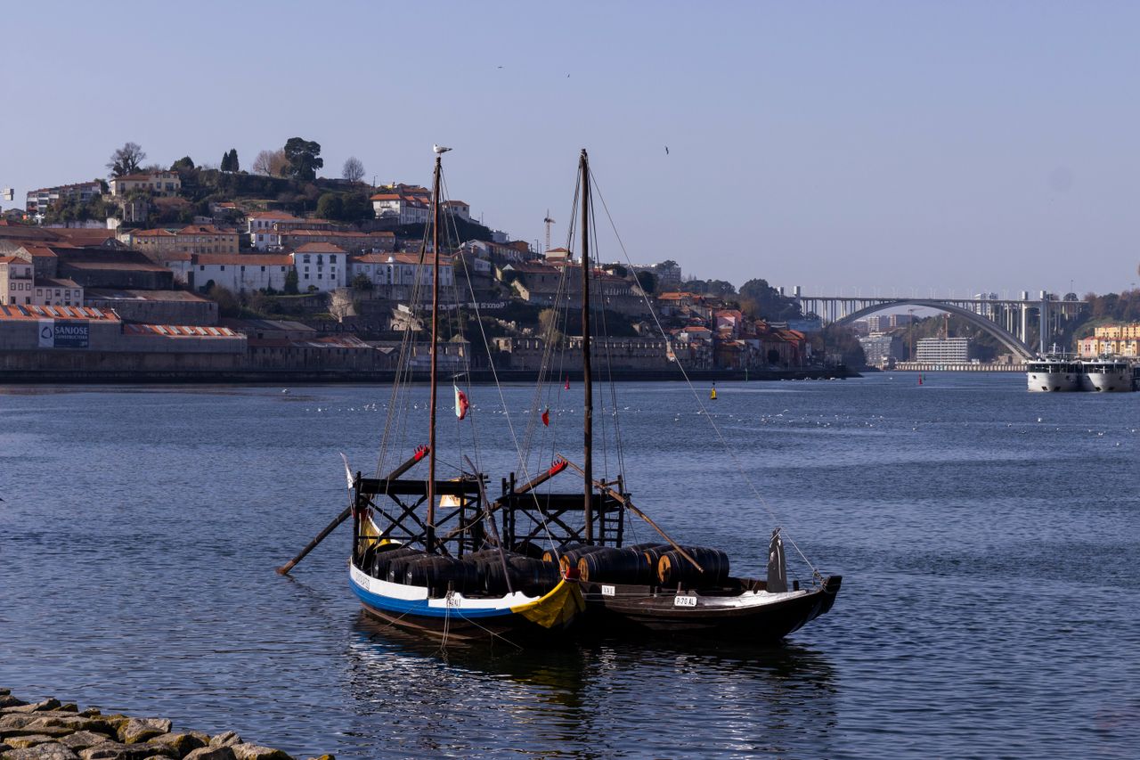 A serene view of the Douro River with traditional rabelo boats and Arrábida Bridge in Porto, Portugal.
