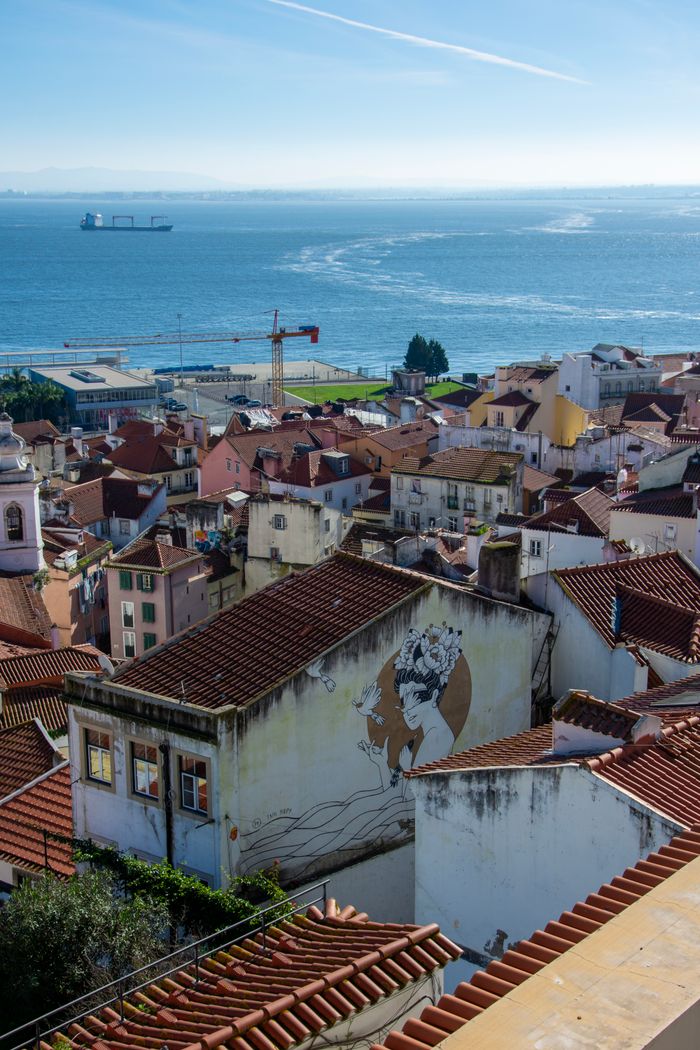 Aerial view of Lisbon's historic rooftops and vibrant street art with the Atlantic Ocean in the background.